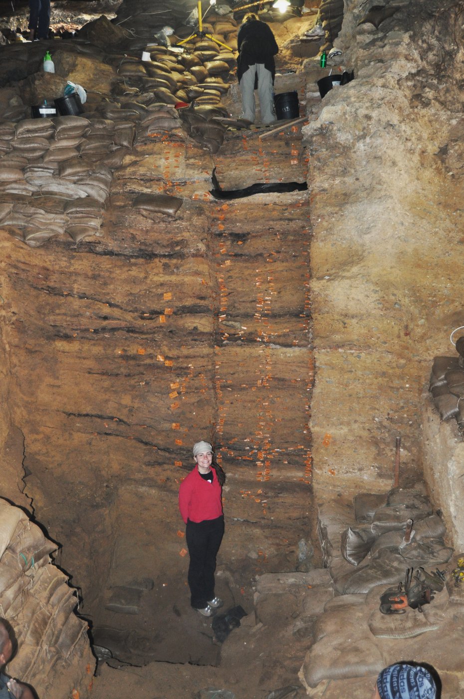 At the base of a deep excavation trench, tagged layers rising above her